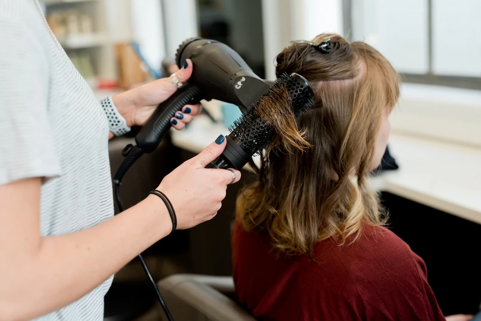 Estilista secando con cepillo el cabello de una clienta en un salón