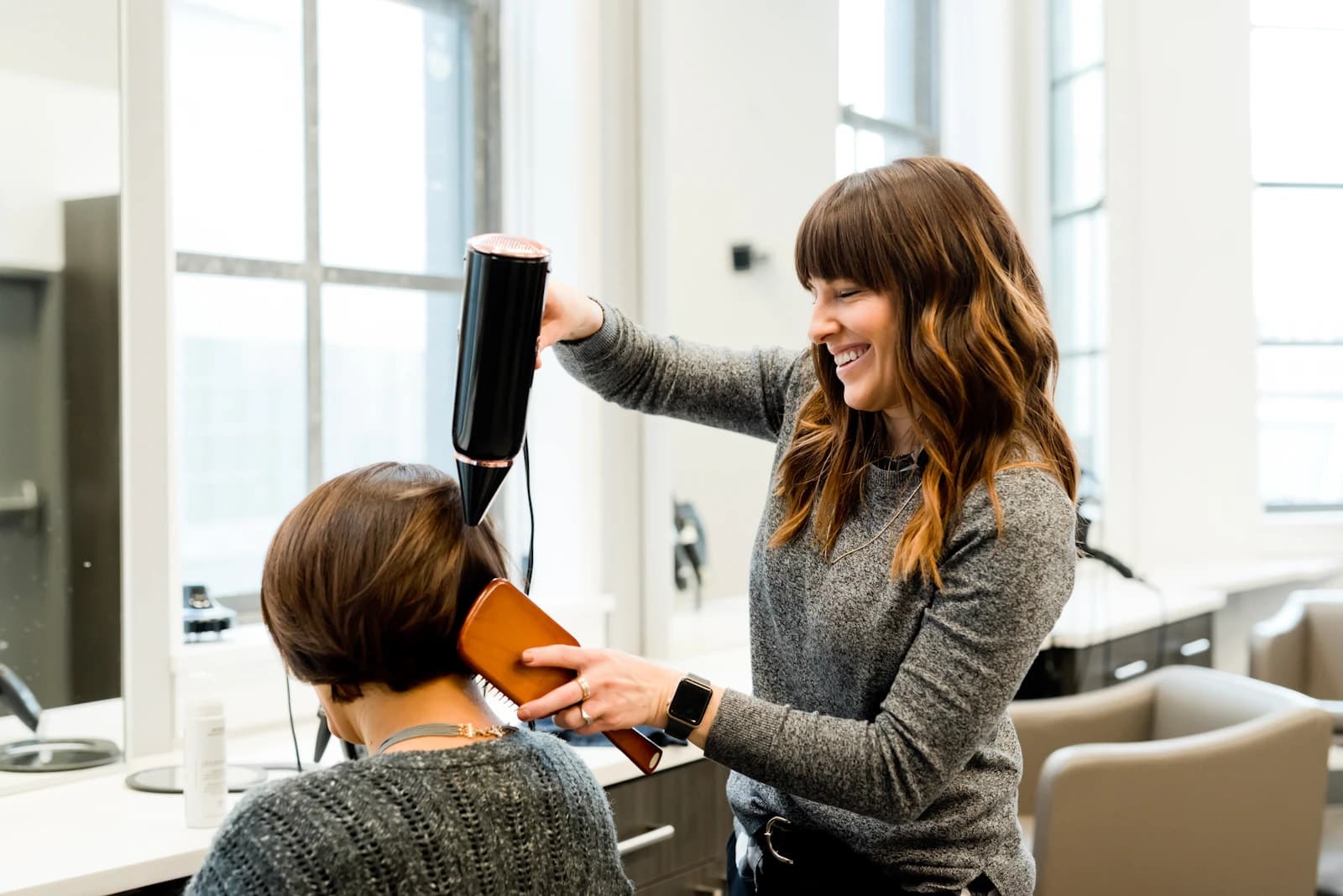 Estilista sonriendo mientras seca el cabello de una clienta en un salón
